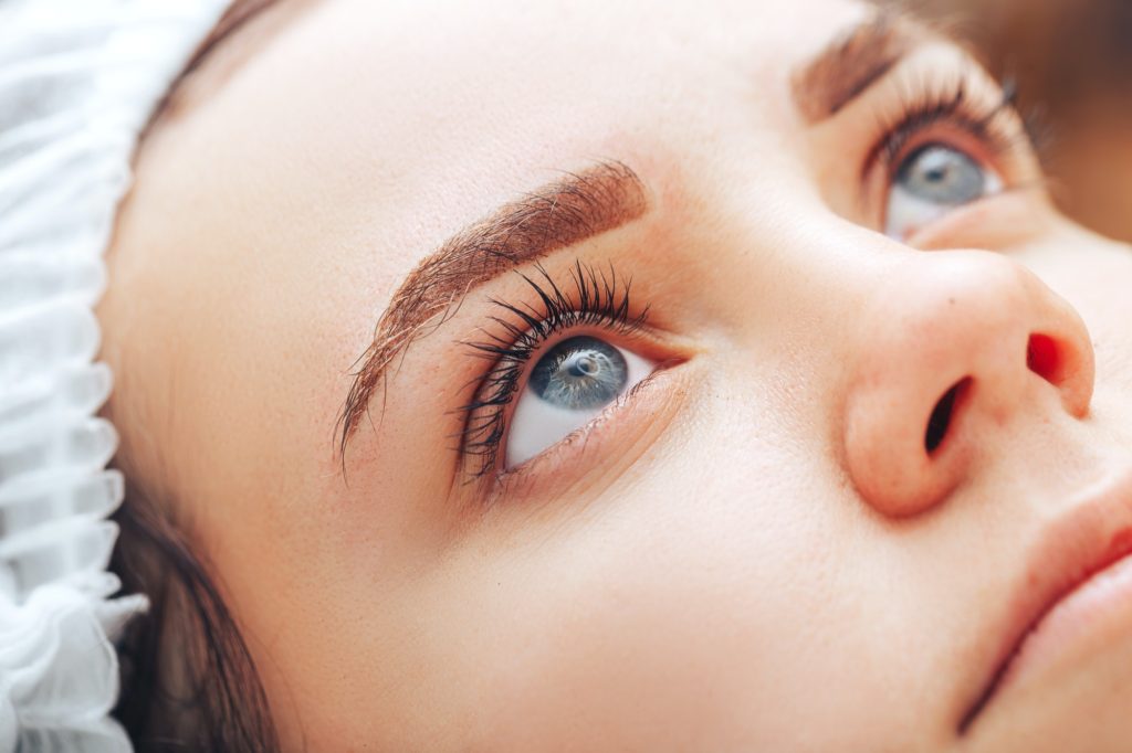 Young woman with beautiful eyebrows after procedure permanent make-up in salon, closeup photo